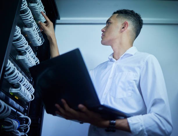 Man, laptop and technician work on server room, data center or database cables check, maintenance or network inspection. Cybersecurity inspection, programmer and person service backup hardware system